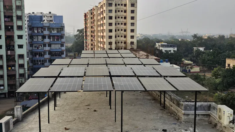 Front view of solar modules on tall steel legs across a flat rooftop, apartment blocks and trees behind.