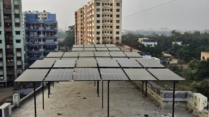 Rows of solar modules on a raised steel structure above a flat rooftop, apartment blocks behind.