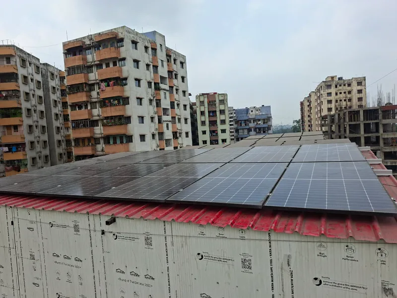 Solar modules covering the red sheet roof of a rooftop shed, apartment blocks around it.